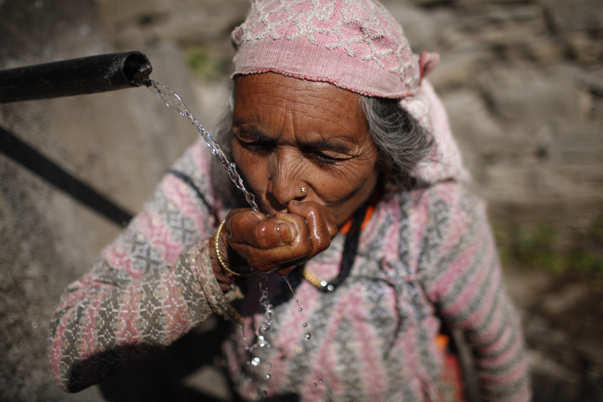 Ganesh Kumari Karki (60) drinks water from a public tap at Dhap village. Photo: Tom van Cakenberghe / IWMI